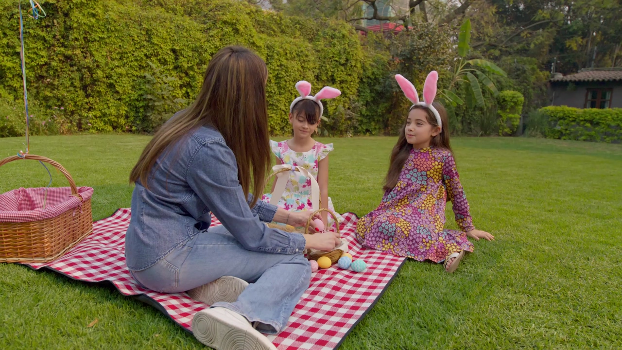 A family celebrating easter during a sunny day at a picnic with easter eggs, bunny ears and baskets
