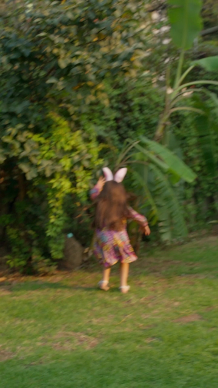 A little girl runs toward the garden bushes and finds a blue eastern egg, the little girl runs with joy after finding an eastern egg hidden in the bushes of the garden