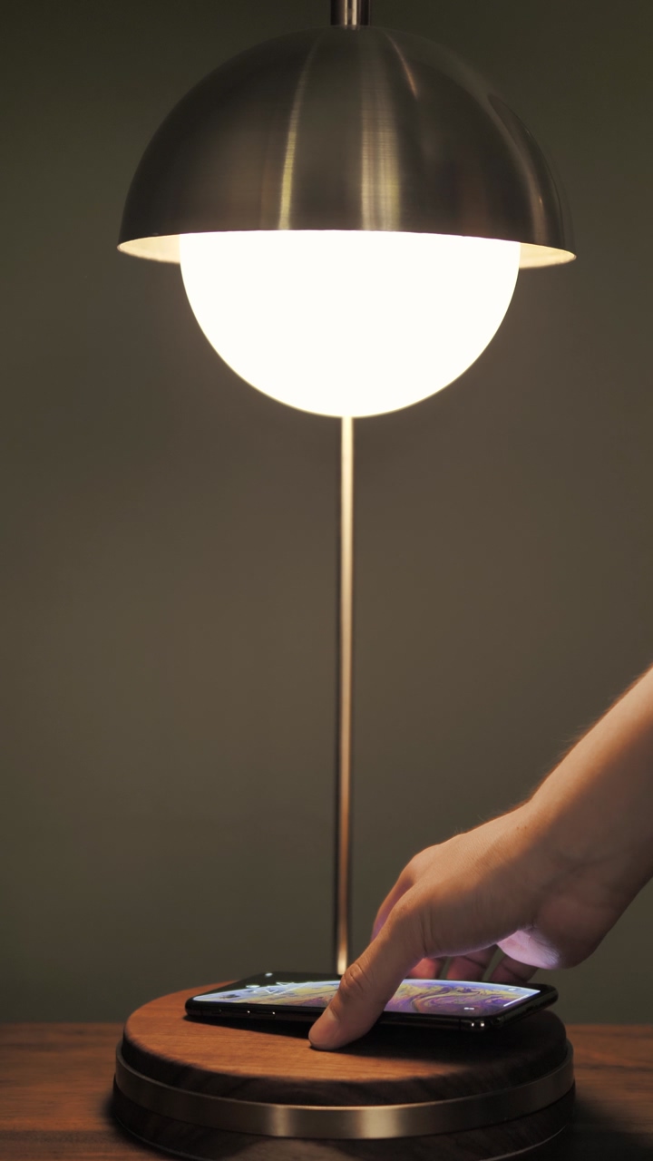 A person's hand puts an iphone under a bureau lamp