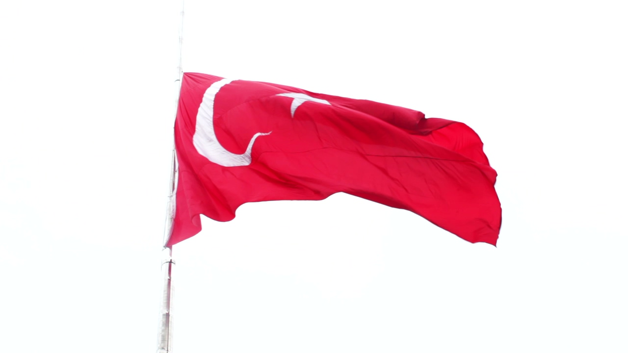 Close shot of the flag of turkey waving on a pole with the sky above it in the background