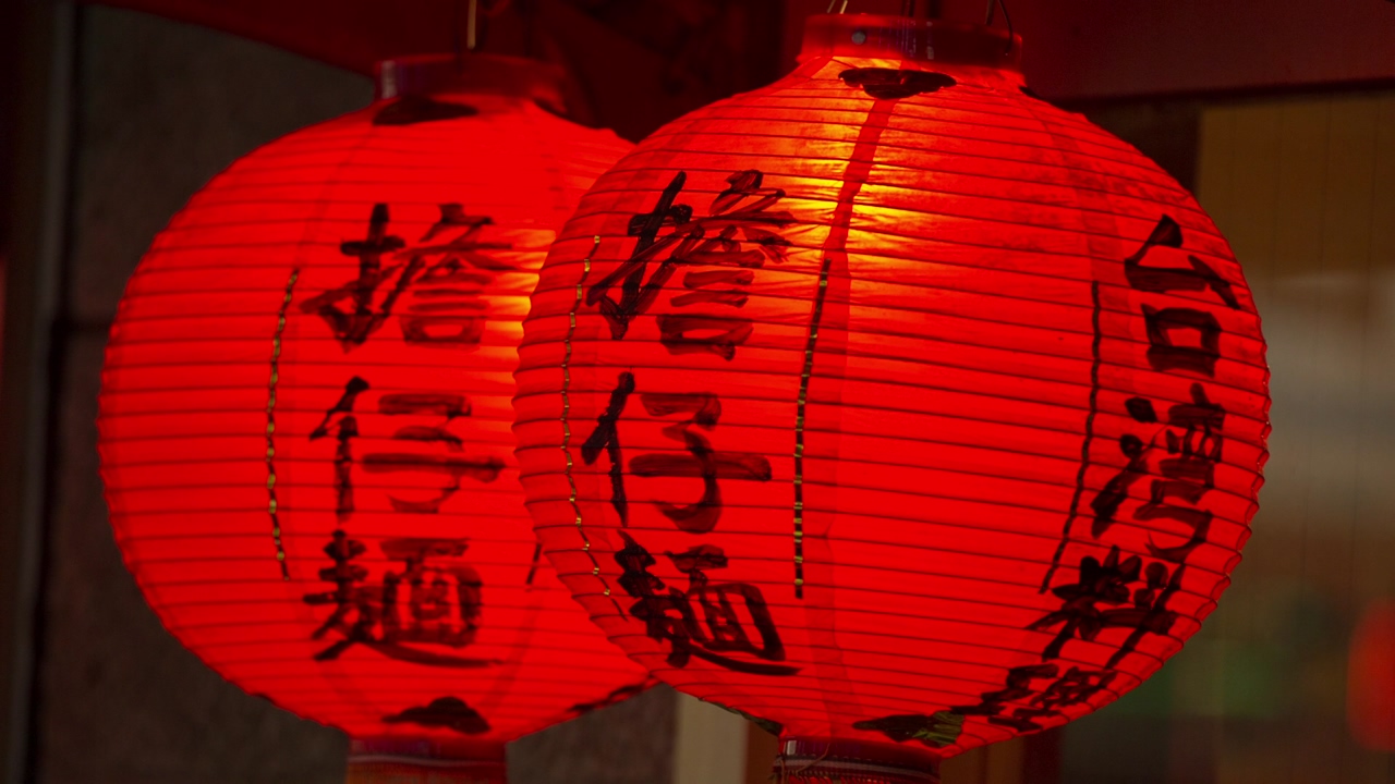 Close up on a pair of circular paper lamps in red, with japanese writing in black