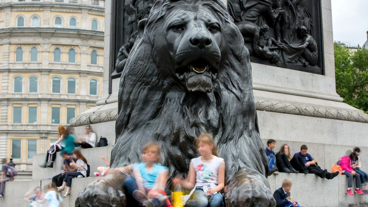 Close-up shot of a giant lion statue at trafalgar square in london on a bright afternoon, as several people walk and sit around to take photos of the statue