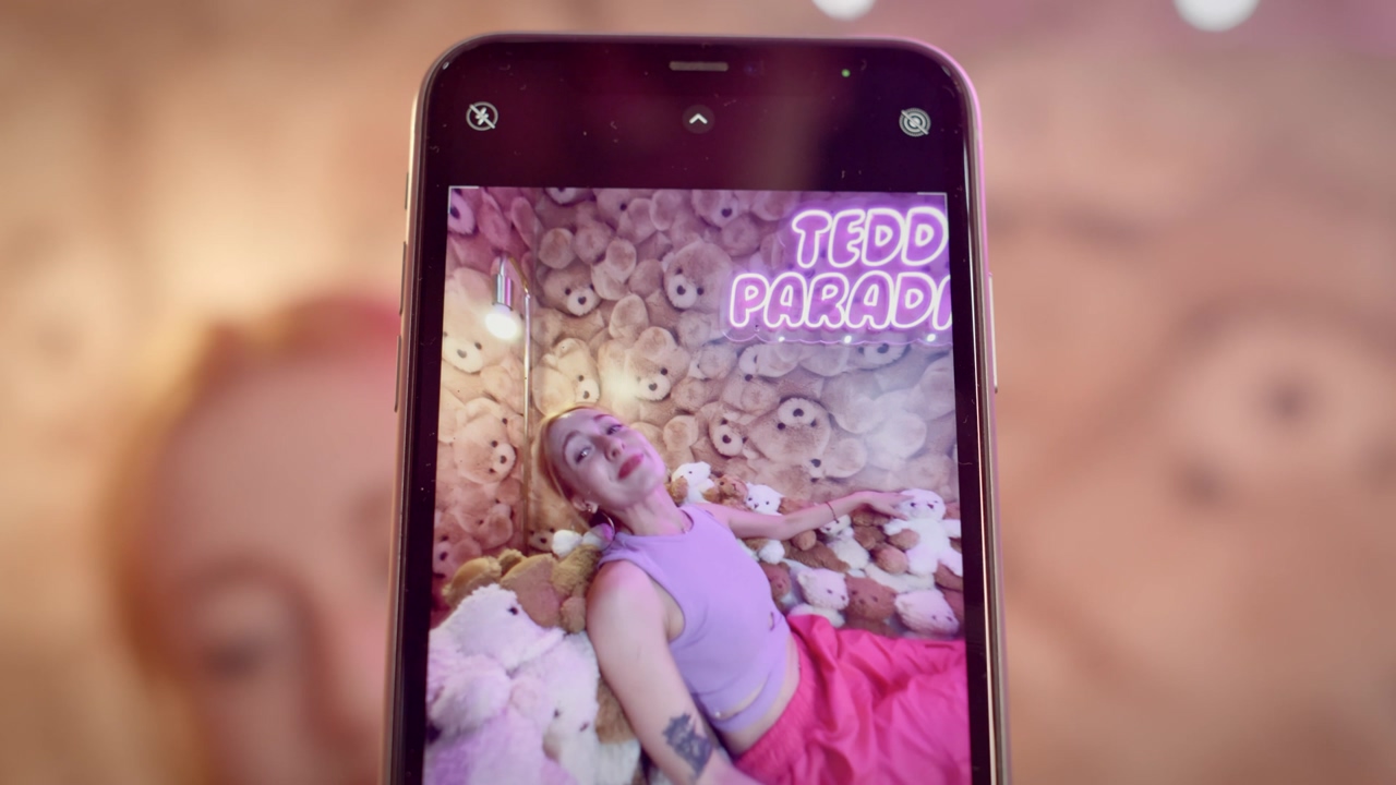 Close up shot of a young woman being recorded in a teddy bear-themed room posing and smiling with a pink neon sign