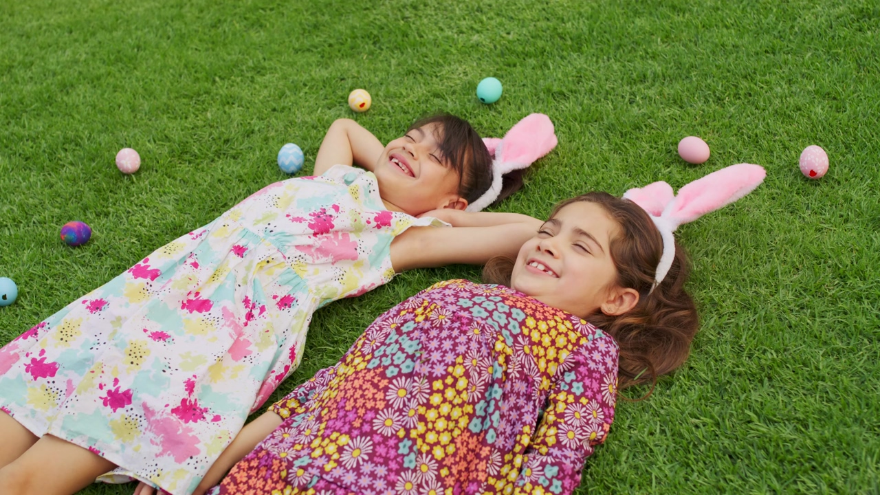 Happy girls lying on the grass in a garden during easter day surrounded by decorated eggs of different colors
