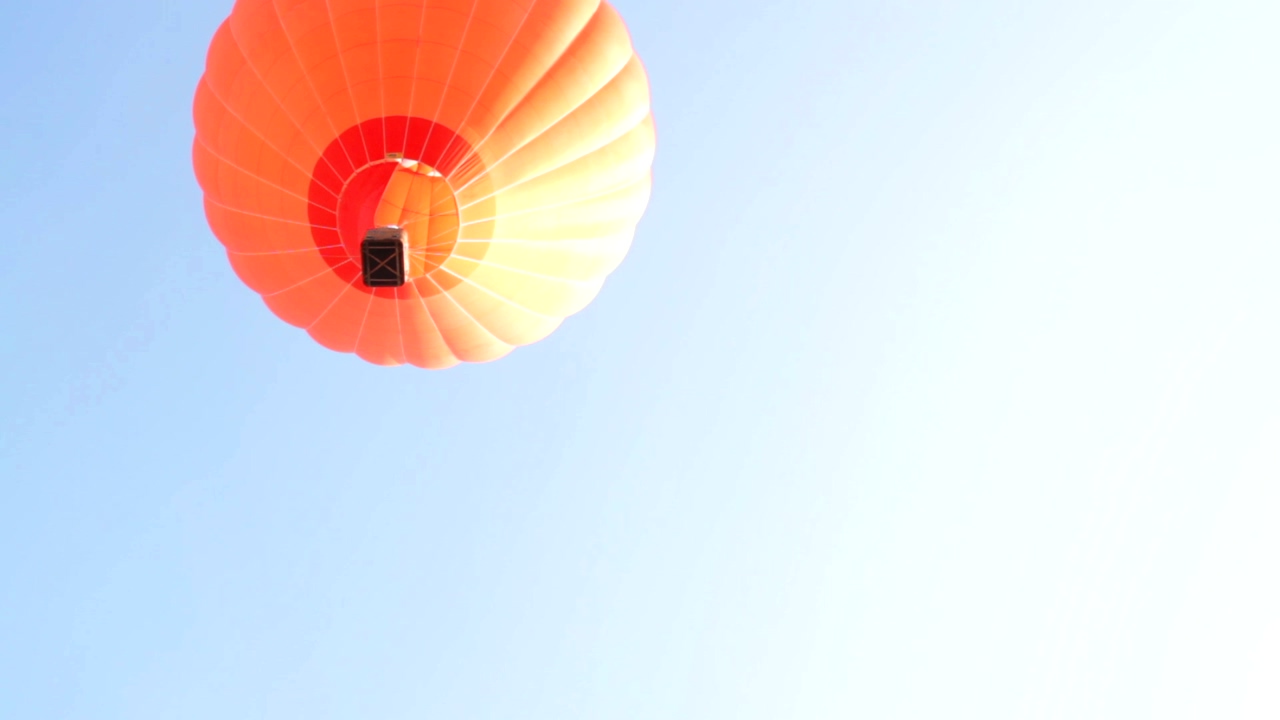 Orange hot air balloon seen from below is flying in the blue sky without clouds