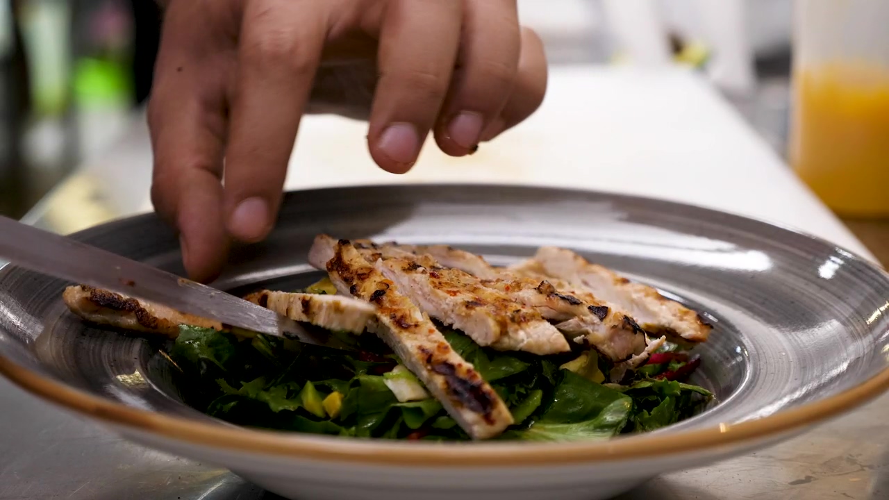 Placing grilled chicken on salad, cooking, salad, and chicken