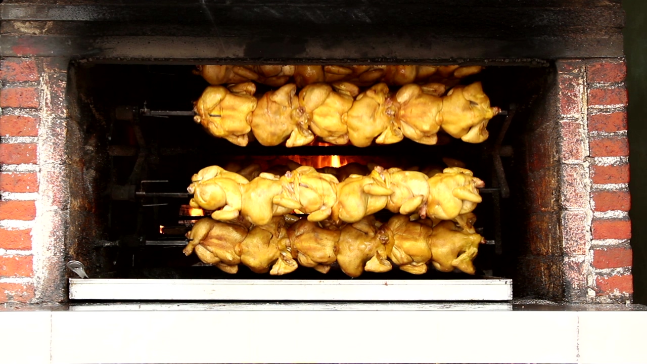Symmetrical shot of a rotary brick chicken oven, with fire and chickens baking inside