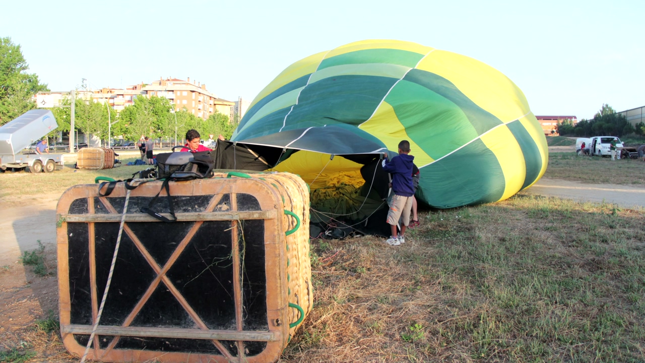 Time lapse of people inflating a green hot air balloon, in the background buildings and trees of the city