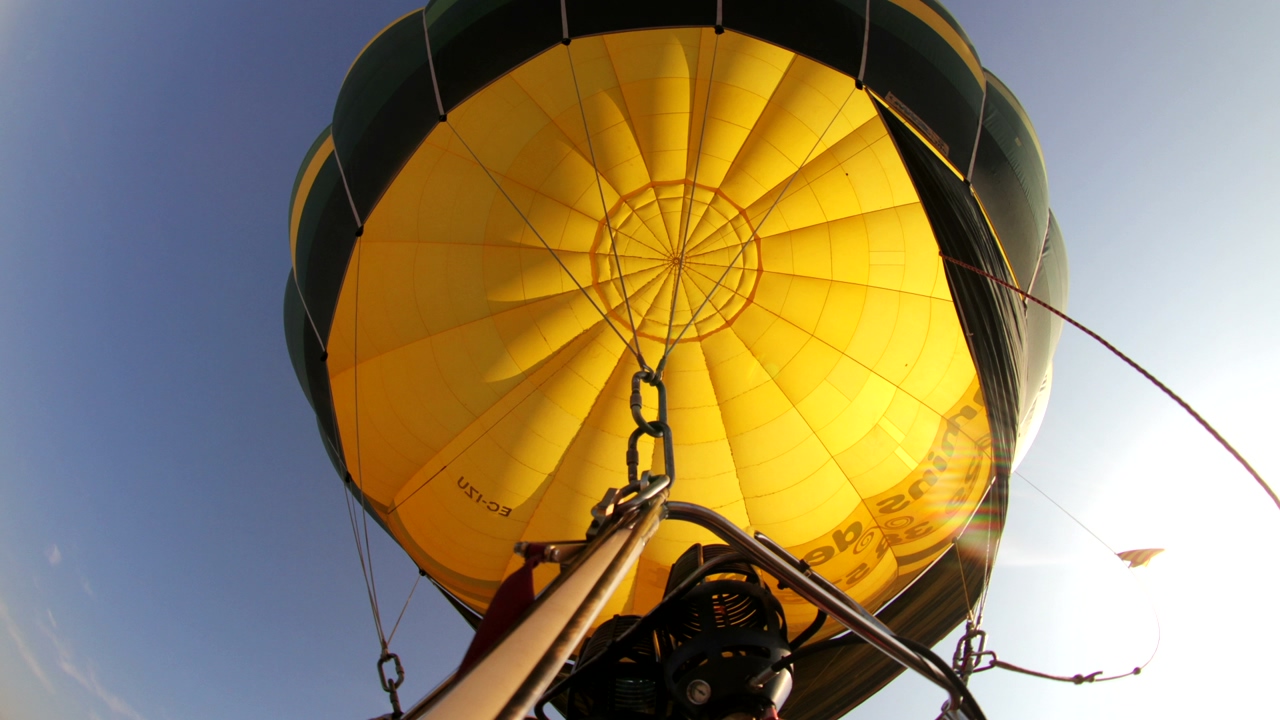 View from below of a yellow hot air balloon while flying in the air, blue sky in the background